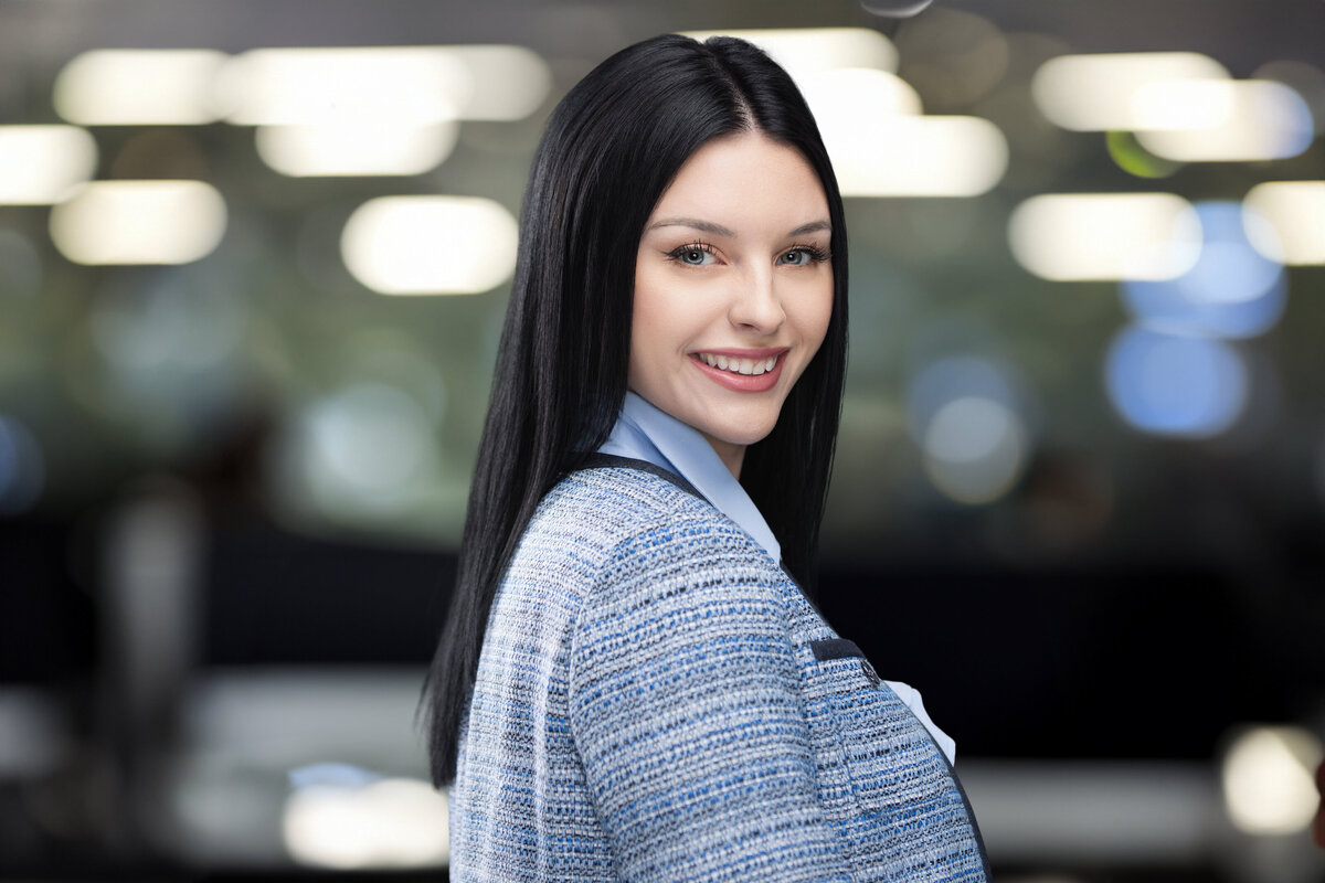 Professional headshot of a woman in Cincinnati with a confident smile. She wears a blue blouse layered under a textured blue blazer, exuding professionalism and approachability. Captured with a blurred office-style background, this image is ideal for corporate and personal branding purposes, showcasing the expertise of Cincinnati headshot photography.