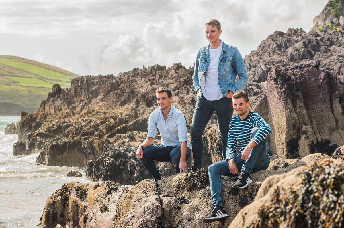 three brothers wearing denim, sitting on a rock overlooking the beach