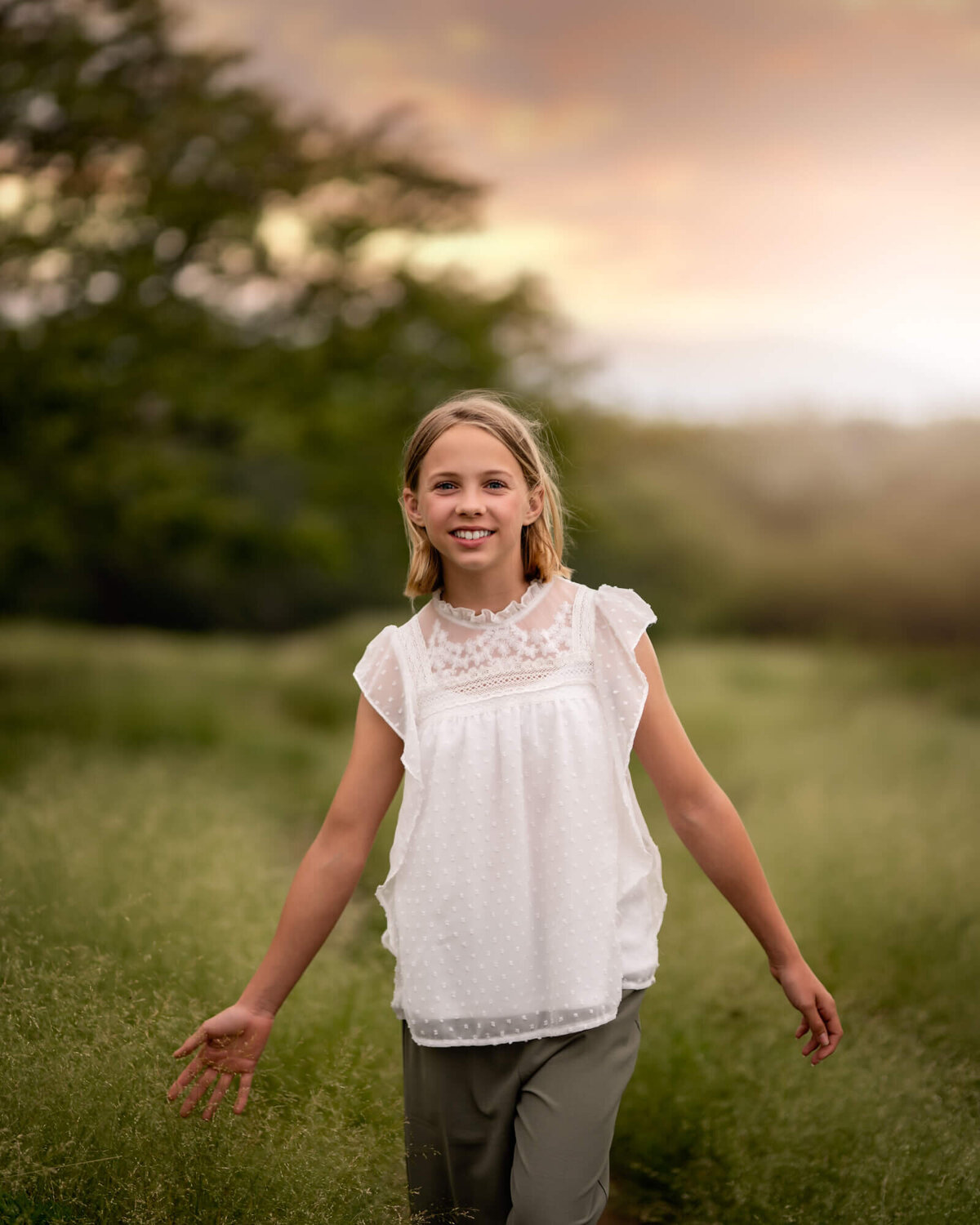 A young girl in a white shirt walking through a trail in tall grass and touching it with her hands
