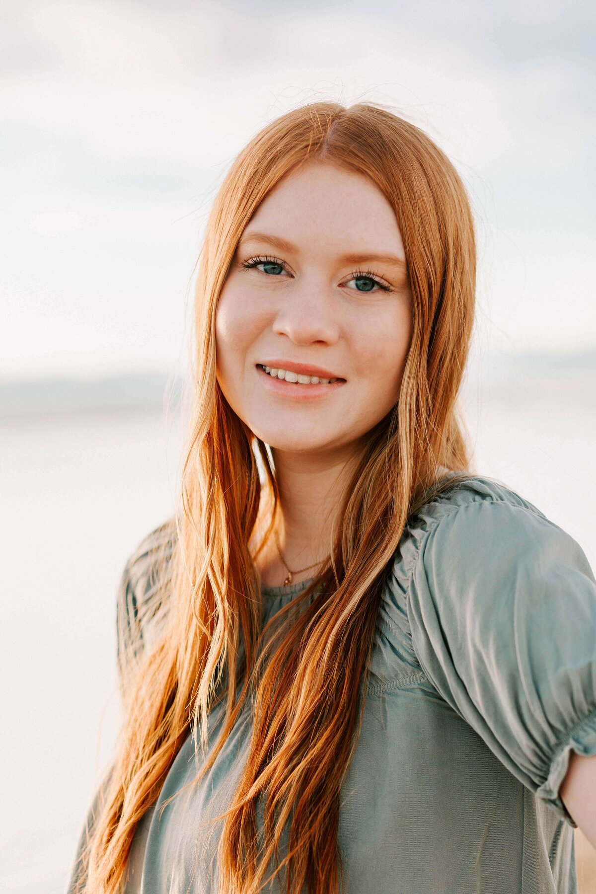 A teenage girl with red hair in a green blouse stands smiling