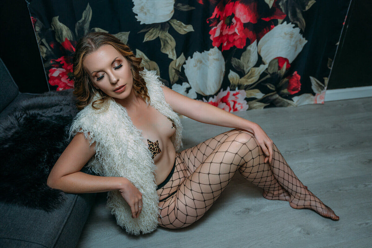 Boudoir portrait  of a woman sitting on the floor  wearing fishnet tights and a fur vest.
