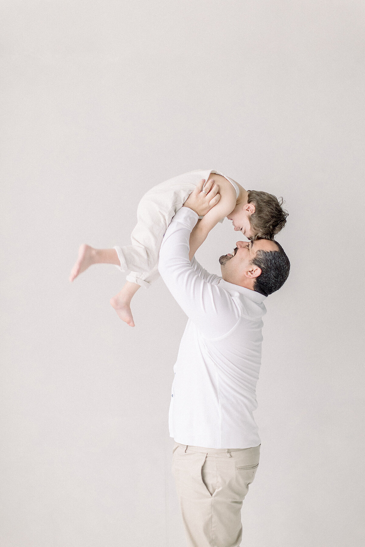 A photo of a dad holding up his young son up in the air as they play around in a Dallas photography studio for their family portraits together.