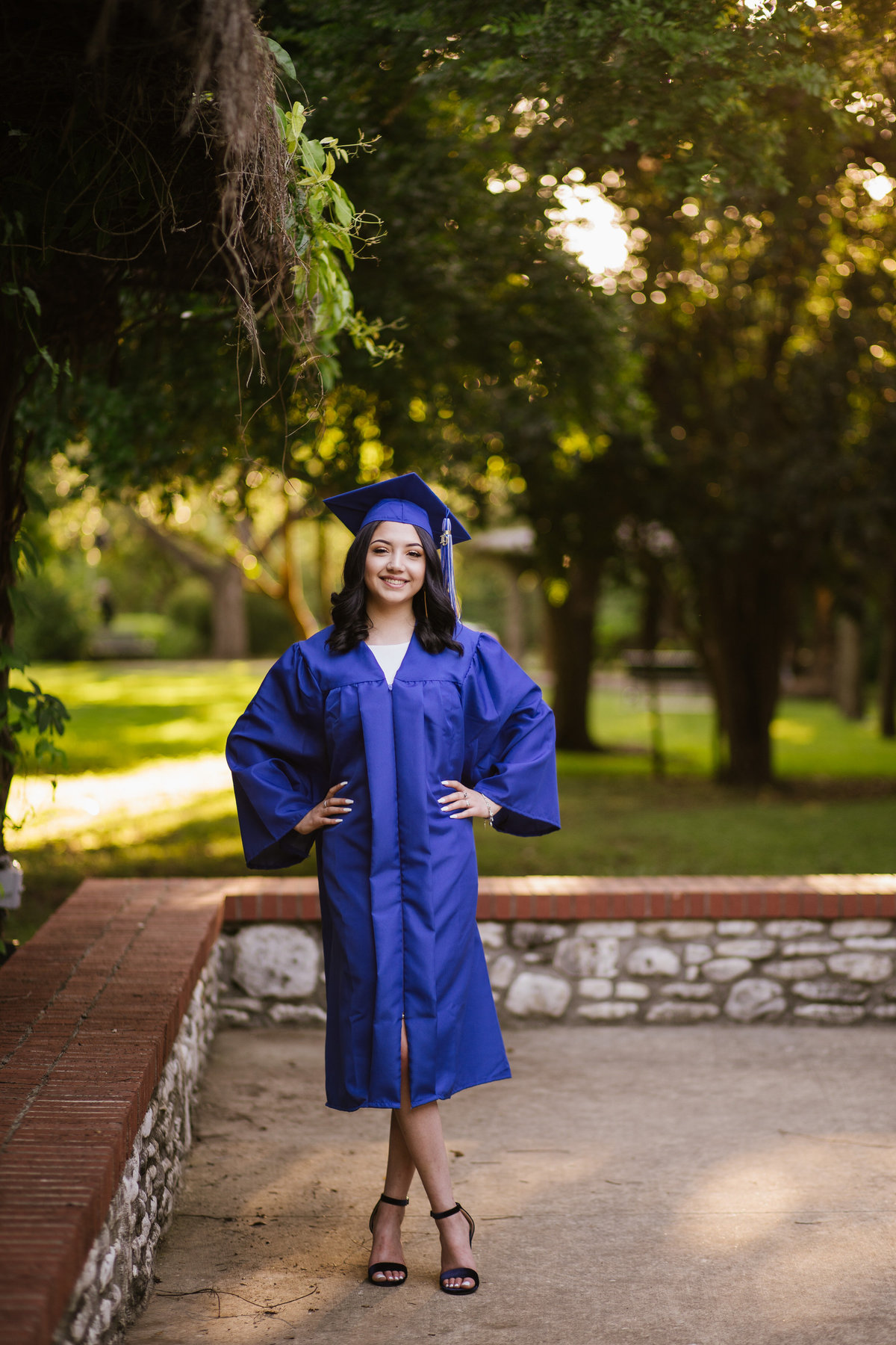 San Antonio high school senior girl in cap and gown with hands on hips by senior photographer