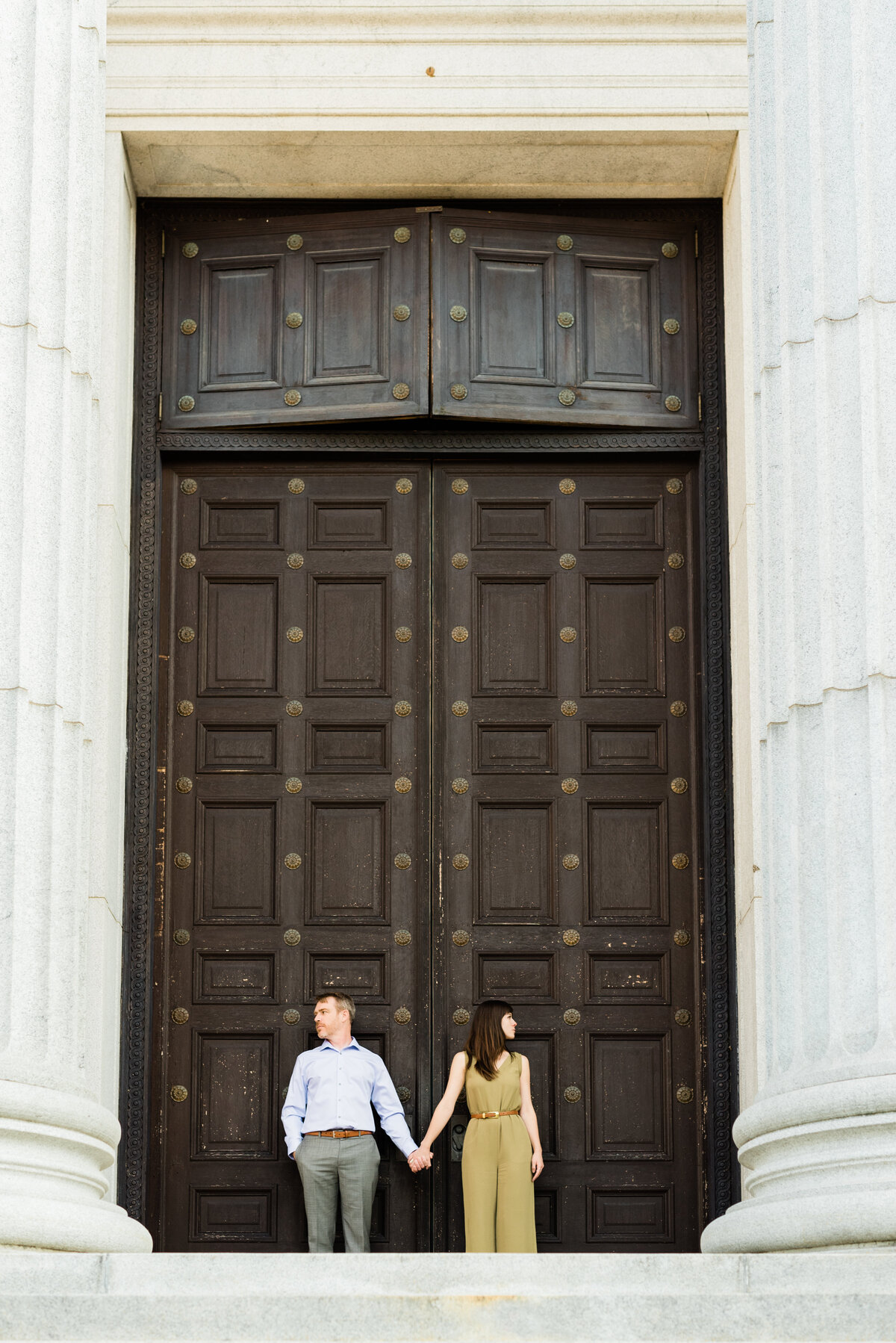 couple standing holding hands in front of large museum door