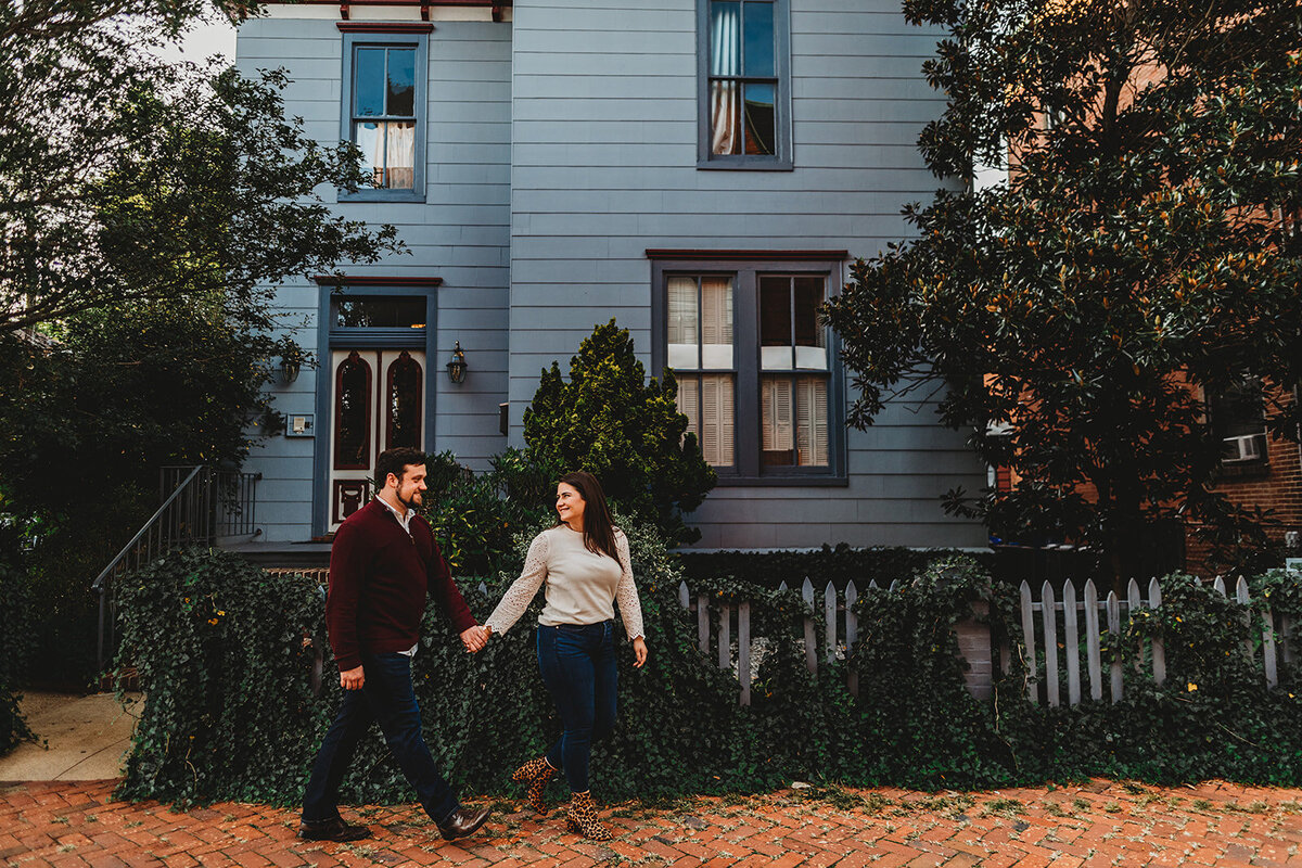 Baltimore photographer captures engagement photos of women holding man's hand and guiding him up a hill in a historic neighborhood for their fall engagement pictures