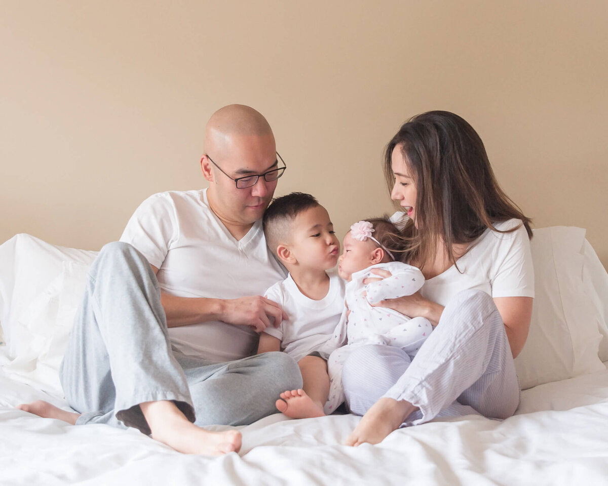 lifestyle family portrait  with family in neutral pajamas with son  kissing new baby sister