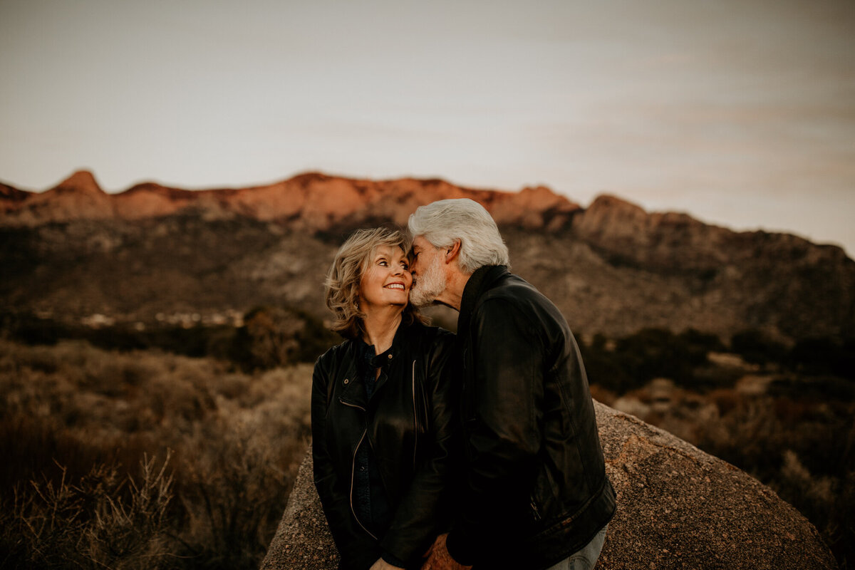 husband kissing wife on the cheek in front of the Sandia mountains