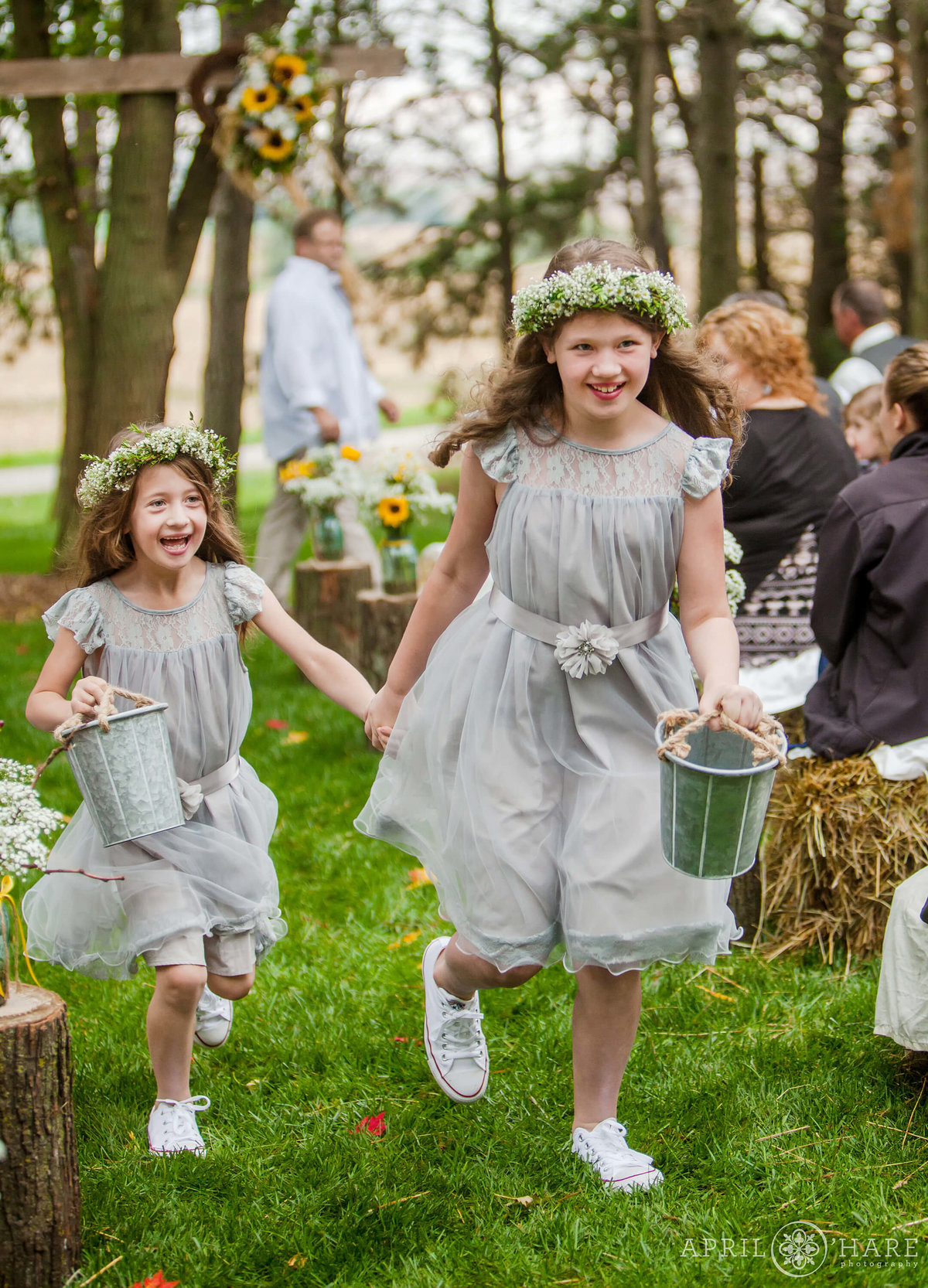 Cute flower girls wearing flower crowns run down the aisle at a private Nebraska Farm Wedding