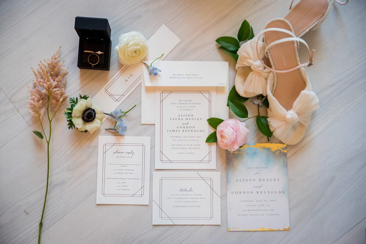 A flat lay of wedding details including invitations, florals, shoes and jewelry, captured by Colorado wedding photographer, Casey Van Horn.