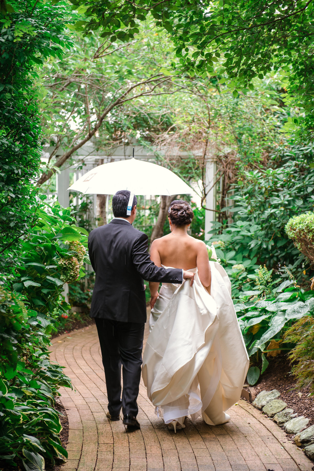 photo of groom holding umbrella and walking with his bride outside The Garden City Hotel