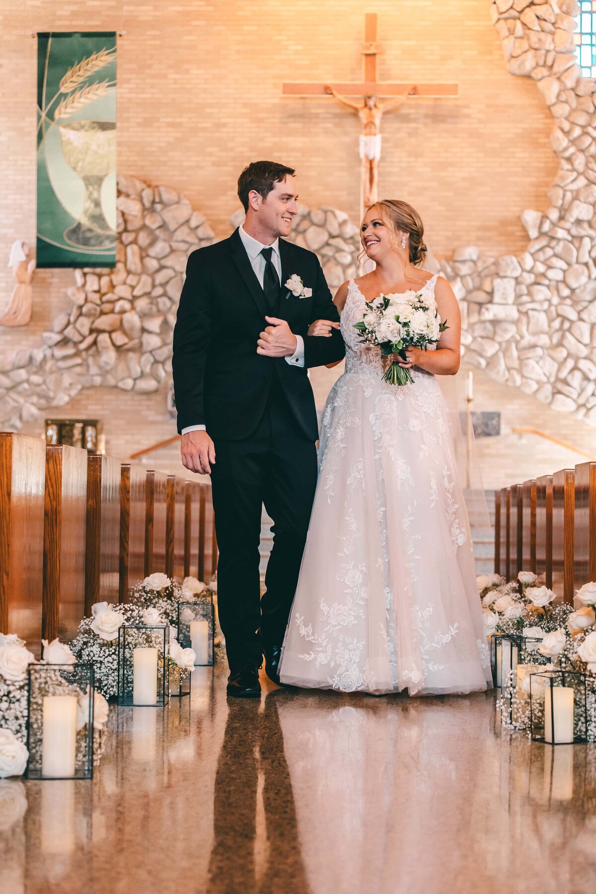 Bride and groom laughing together while walking down the aisle in a church adorned with candles and a cross, as organized by a wedding coordinator in Iowa.