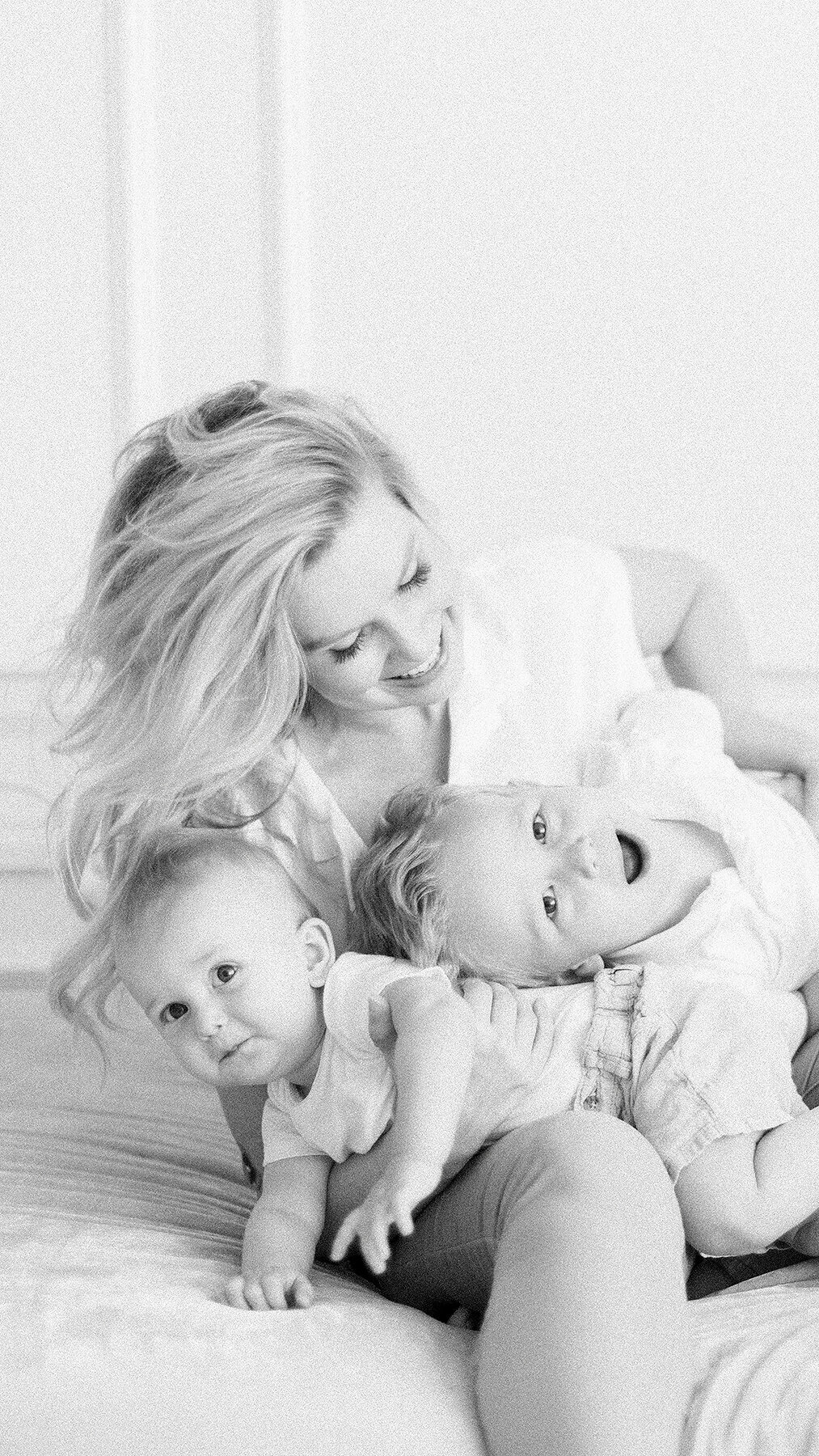 A fun black and white close up photo of a mother and her two kids playing on a bed.