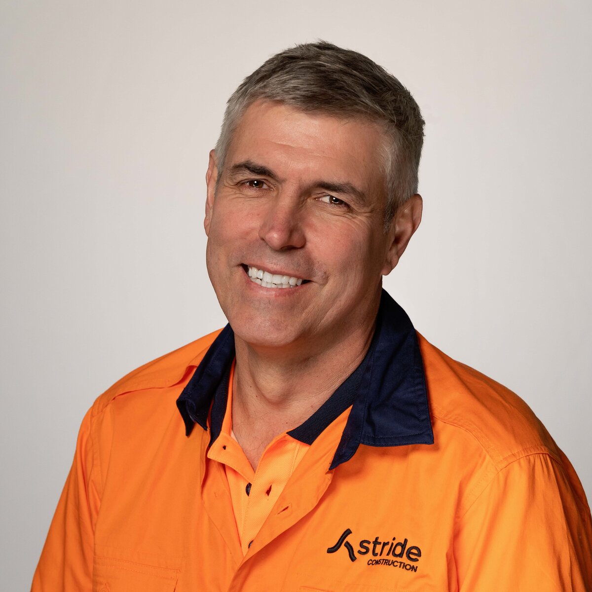 studio headshot of male with grey hair wearing fluro orange safety shirt