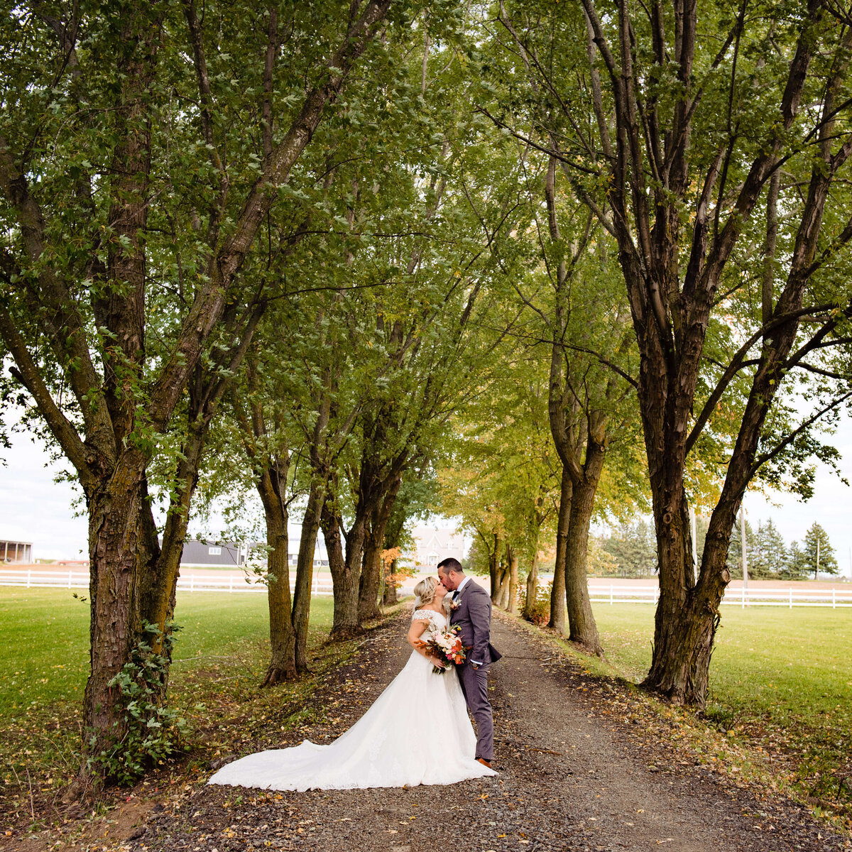 a bride and groom kiss in a tree-lined laneway showing fall colours during their Ottawa wedding photography
