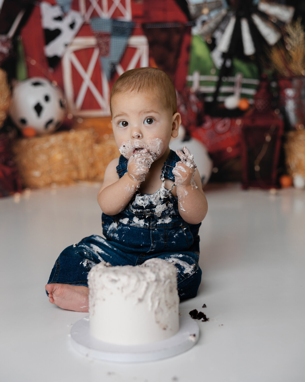 Cute baby boy surrounded by hay bales and cow balloons during a cake smash photo shoot. Photograph by Yucaipa cake smash photographer Kaitlyn Dawn Photography.