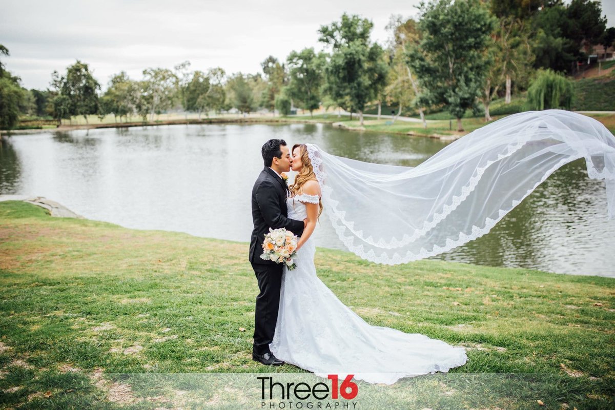 Bride and Groom kiss by the lake at Hotel Fullerton as her long veil blows in the wind