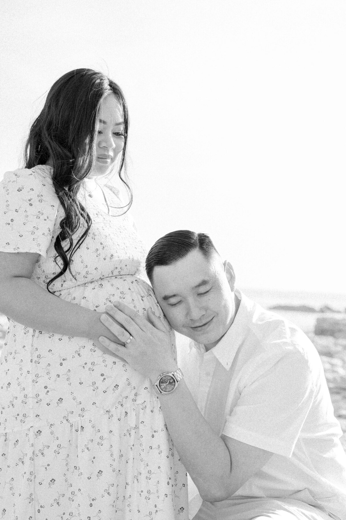 Dad listening to heartbeat in mom's belly at beach photoshoot