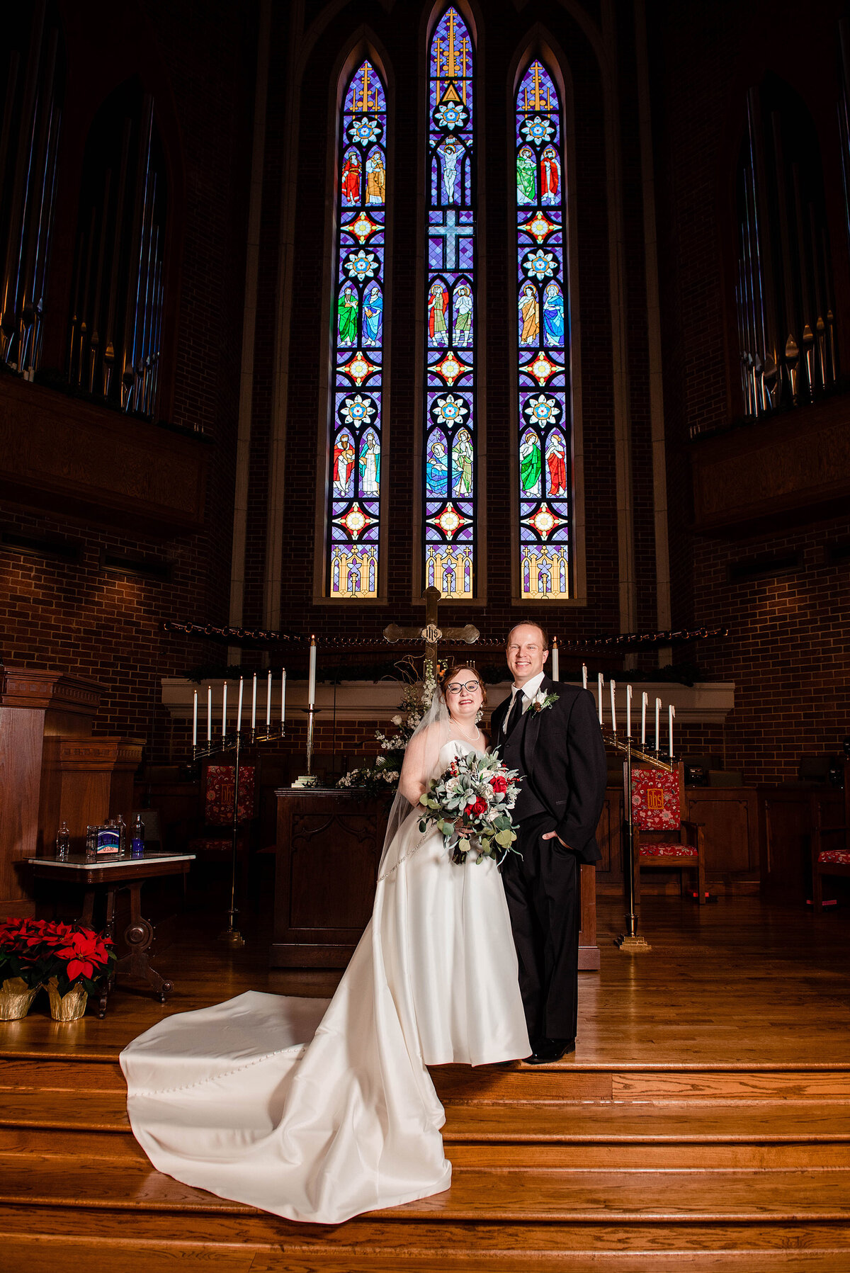 Formal photo of bride and groom standing at church alter with stained glass behind them