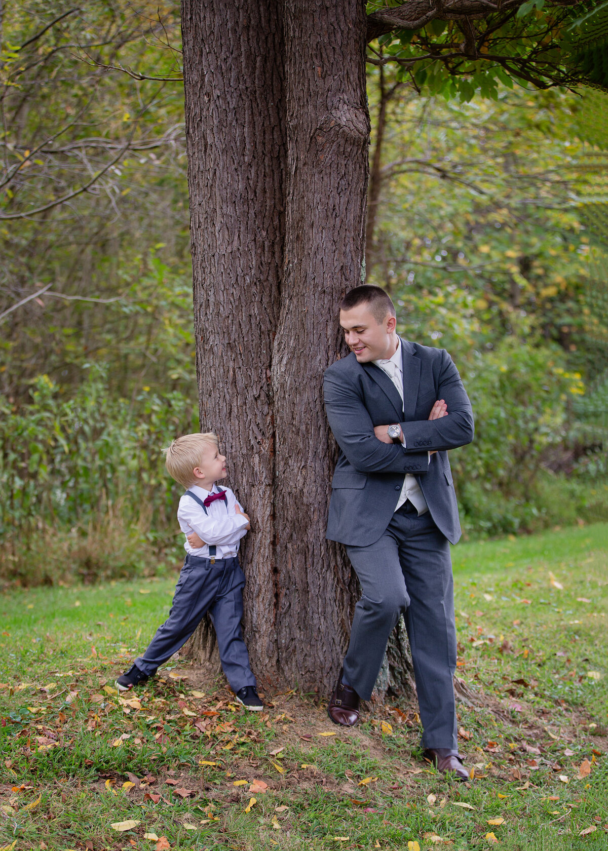 groom and ring bearer with arms crossed looking at each other by tree