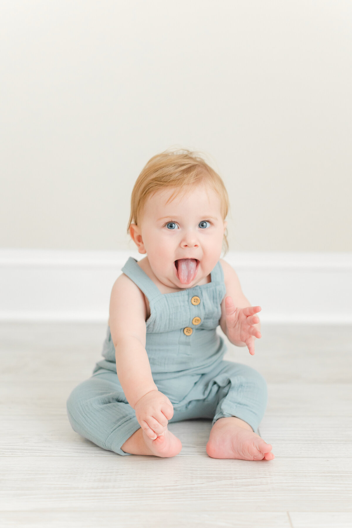 A Baby Photography photo in Northern Virginia of a silly baby boy sitting on the floor sticking his tongue out