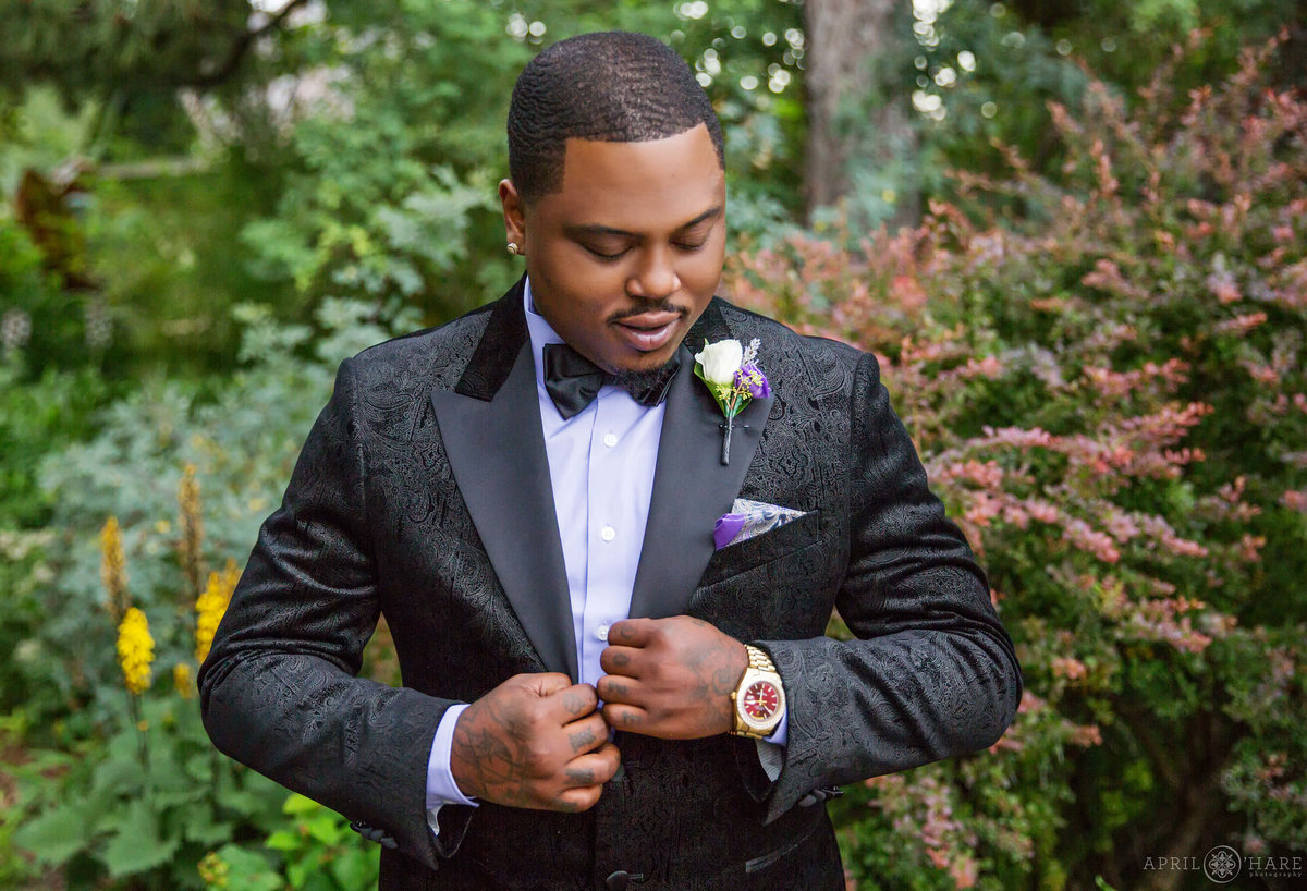 African American Groom with tattoos in a black tux preps for his wedding day at Denver Botanic Gardens in Colorado