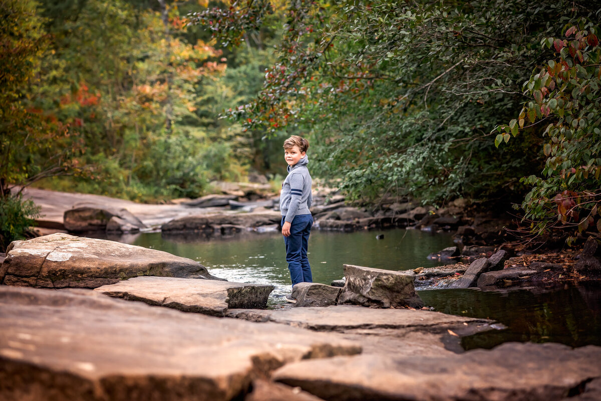 A boy stands in the water at Line Creek in Fayetteville, GA while he looks back at the camera and smiles.