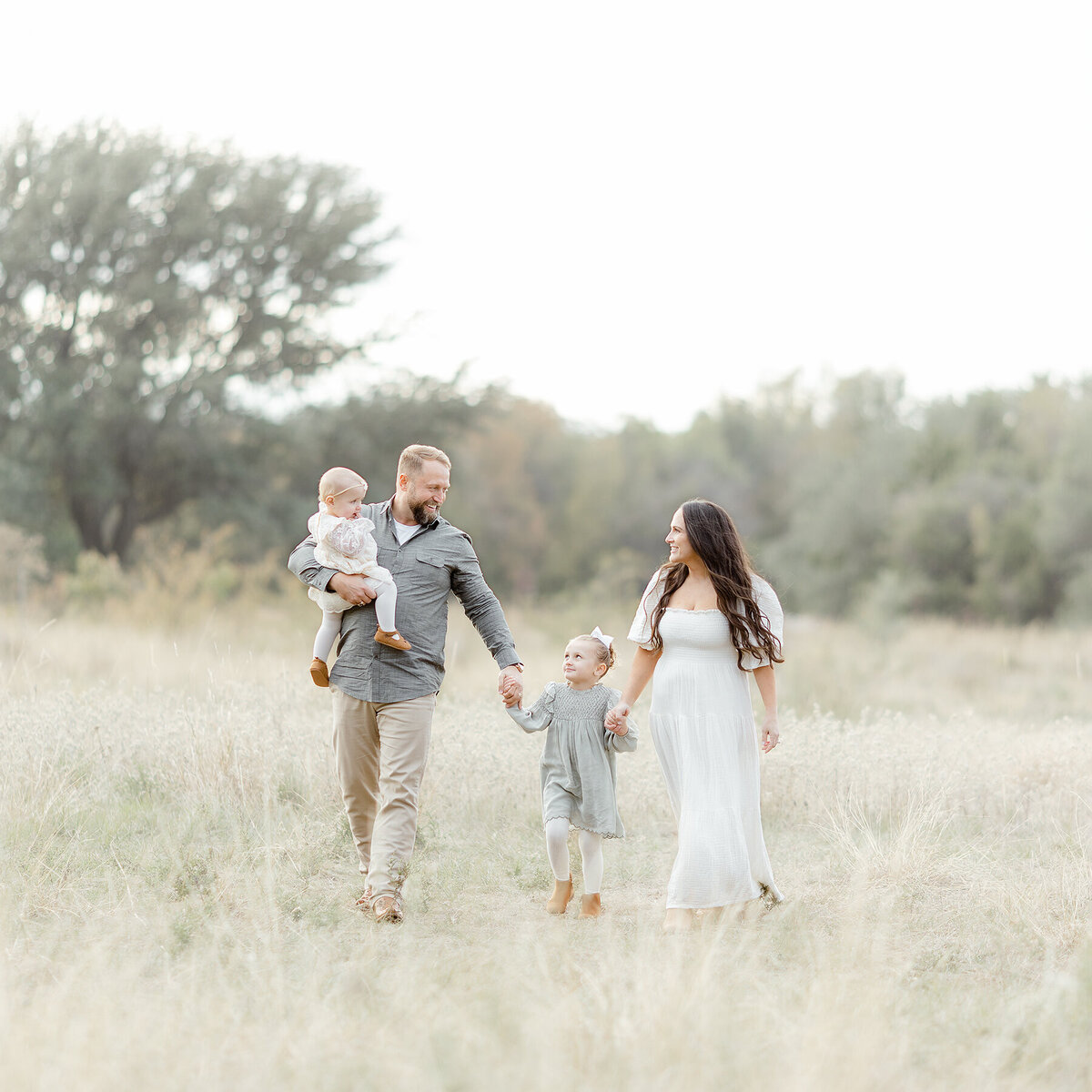 A Dallas family of 4 photo taken while they are walking through a open field at a local Dallas/Fort Worth park taken by a Dallas Family Photographer.