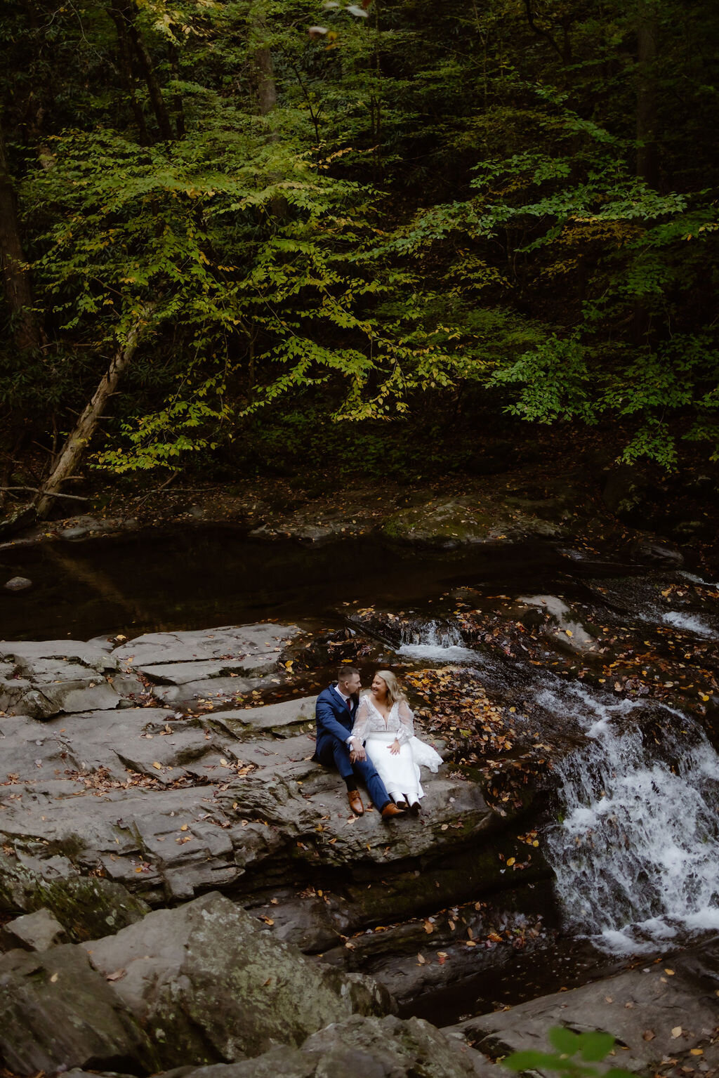 Cades Cove waterfall wedding photos with bride and groom sitting on the top of the waterfall in the woods photographed by Gatlinburg photographers 