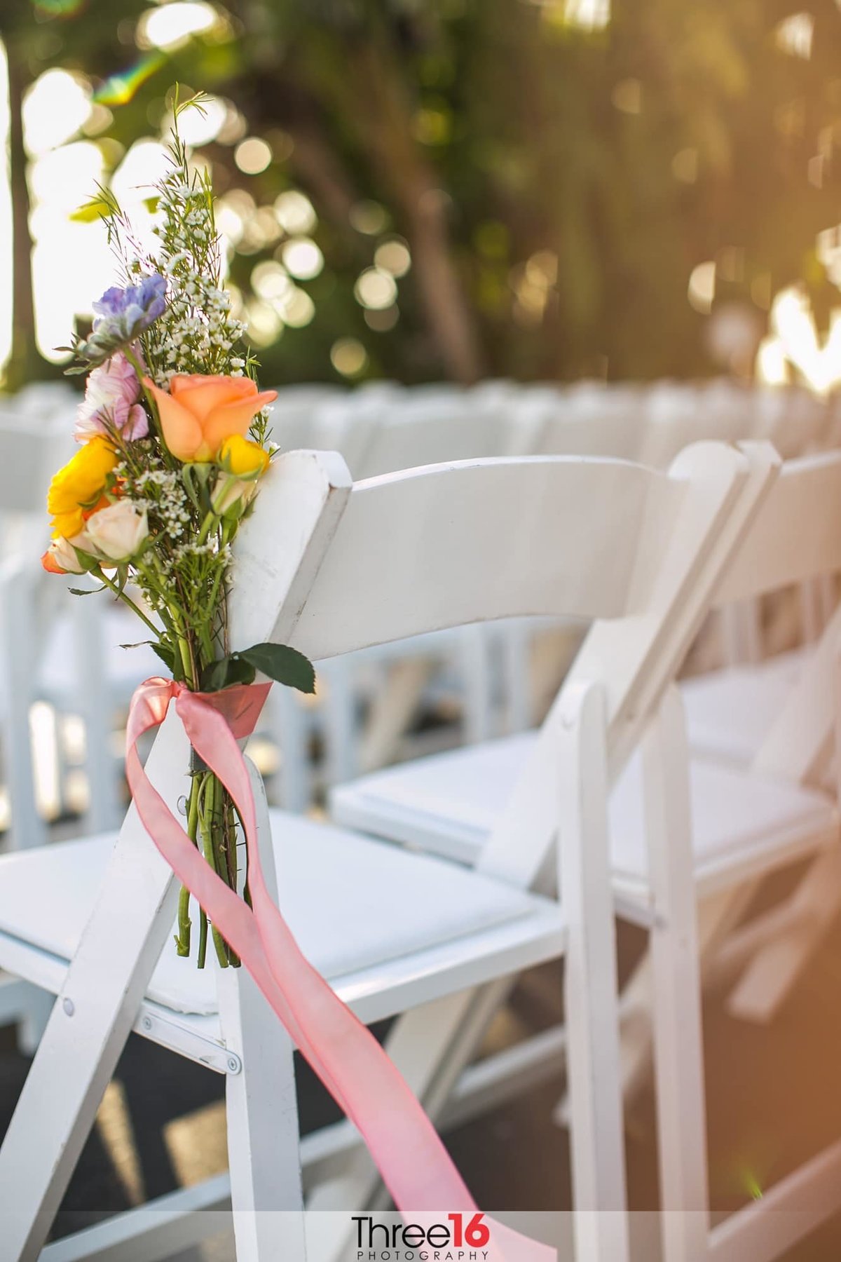 Flowers are attached to the end chair closest to the wedding aisle tied with pink ribbon
