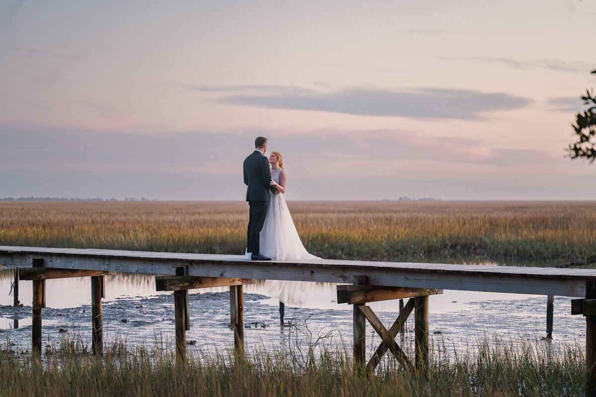 A bride and groom enjoying the sunset overlooking the water on a bridge during their wedding day as they enjoy their Raleigh wedding photos