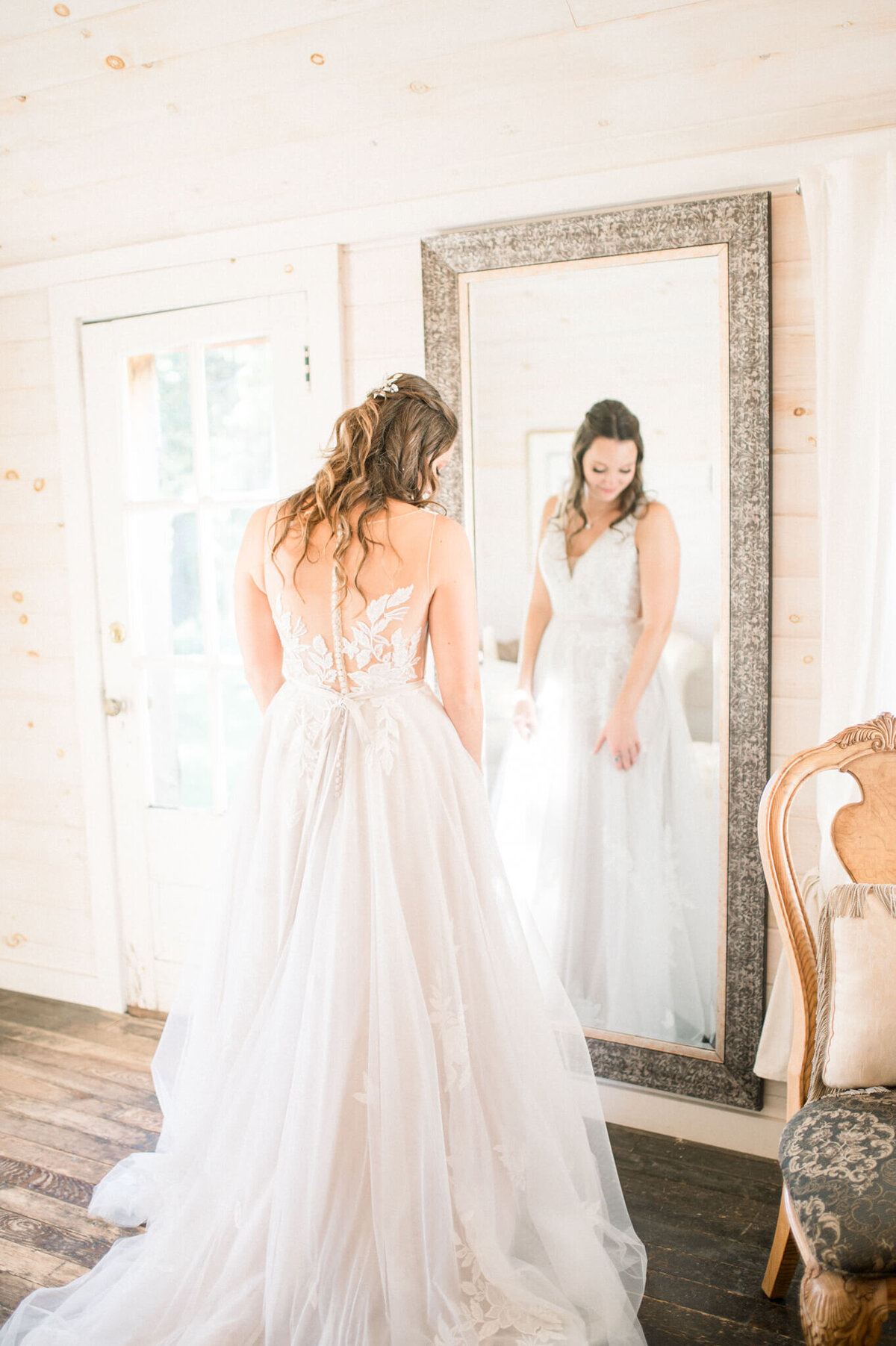 Bride looking at mirror and  fluffing her dress. Captured by Toronto wedding photographer