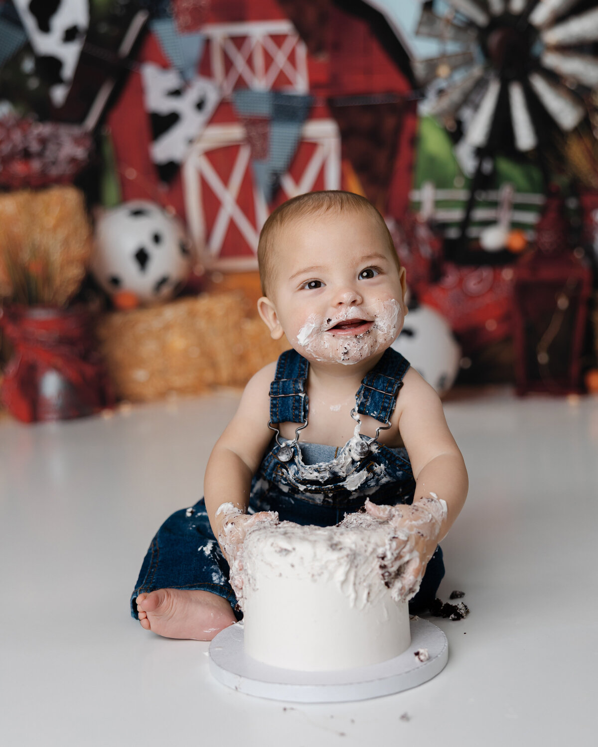 Farm-themed first birthday session with a baby boy digging into his cake, smiling with frosting all over. Photograph by Yucaipa cake smash photographer Kaitlyn Dawn Photography.