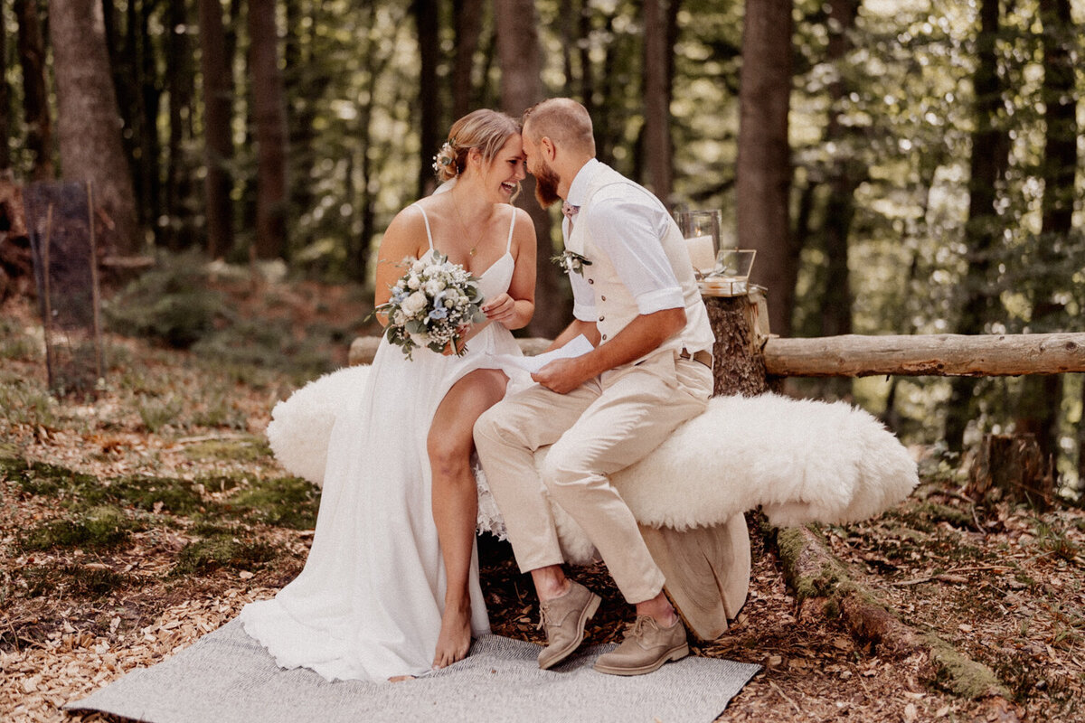 Brautpaar bei innigem Moment auf Waldsitzbank – freie Boho-Trauung im Wald

