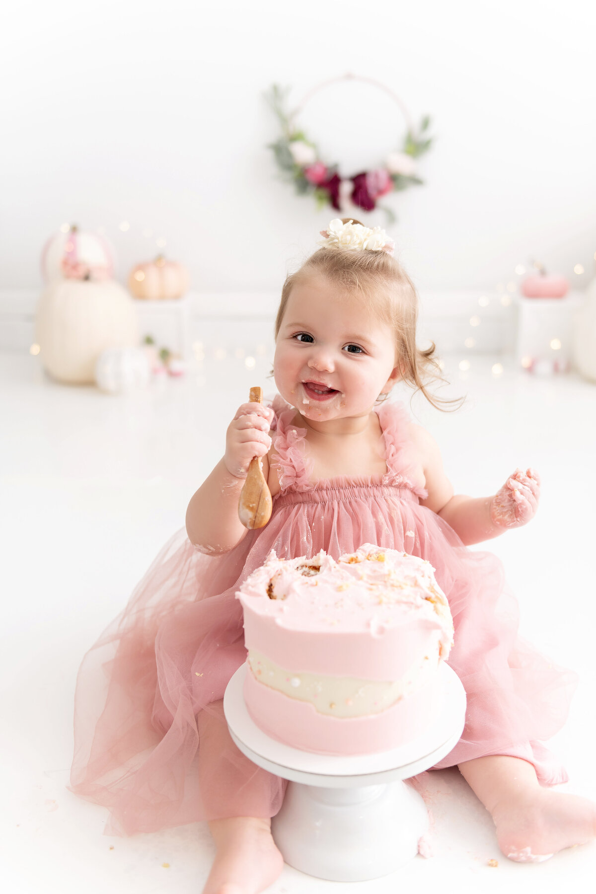 A childrens photographer Atlanta set up a cake for a toddler girl in a pink dress to smash