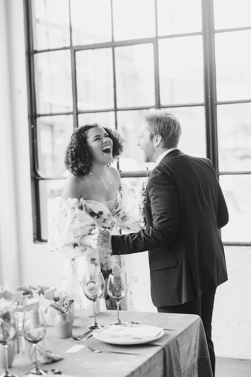 Black and white image of newlyweds laughing hysterically during their wedding reception