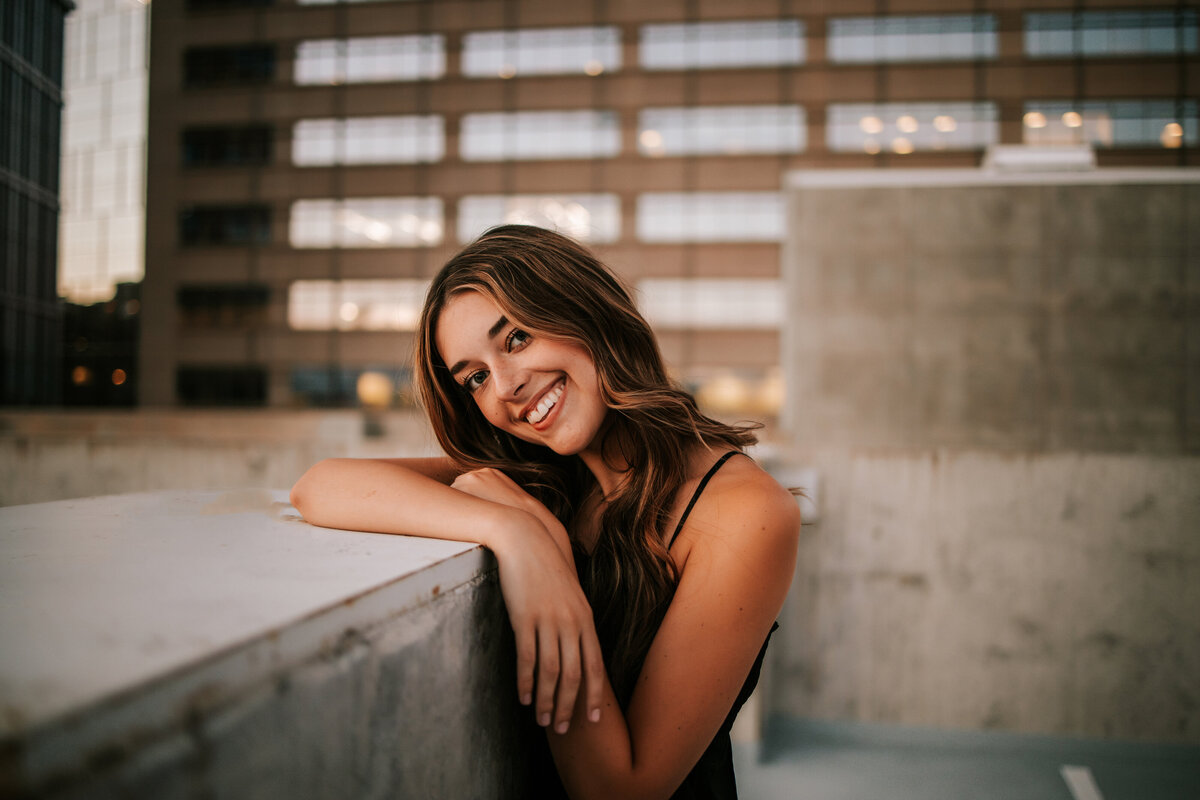 girl leans against cement block on top of rooftop for urban denver senior photos