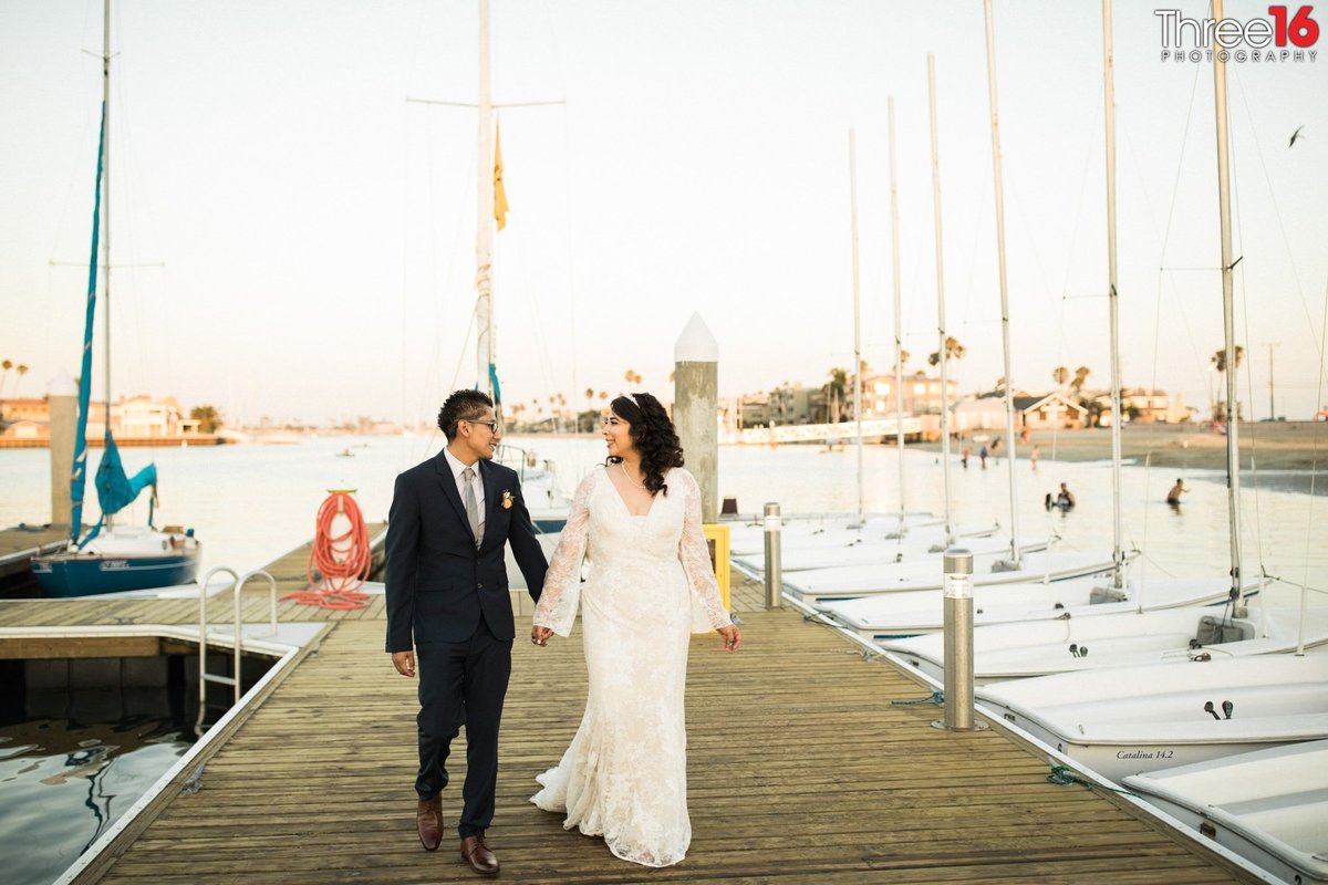 Bride and Groom walk along a Long Beach Harbor deck holding hands