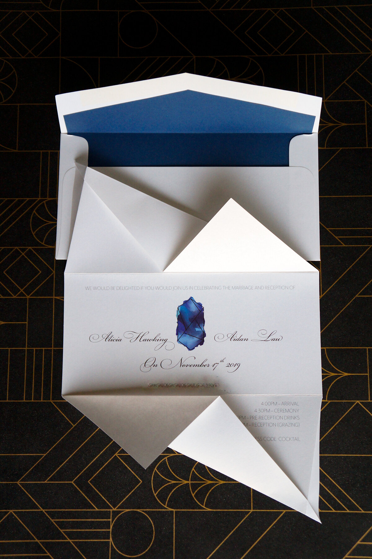 Unfolded origami wedding invitation with blue sapphire graphic and cursive script font