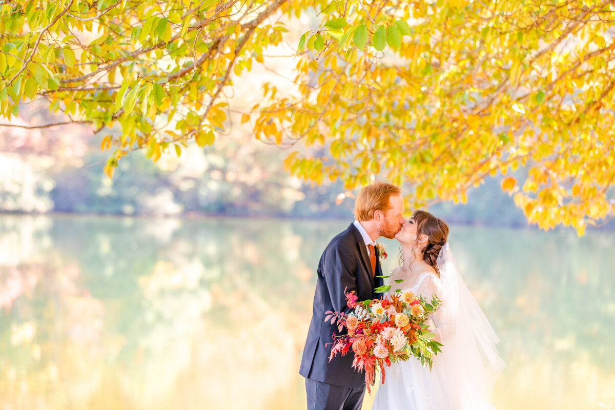 bride and groom kissing by the water under a tree