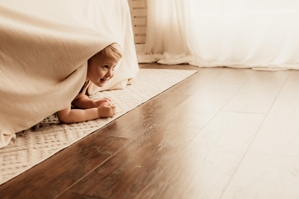 Little boy playing hide and seek under a bed.