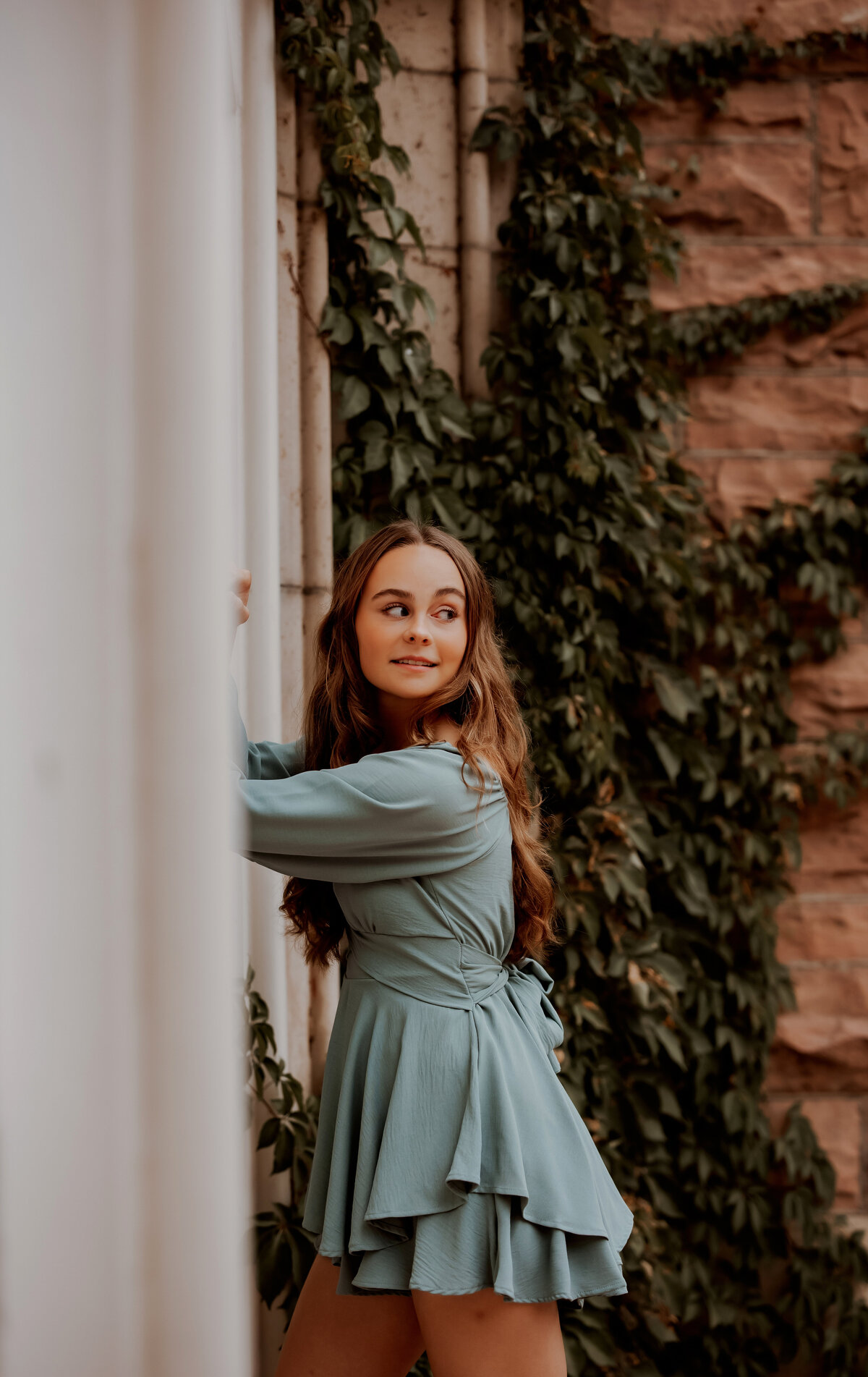 senior girl leans against white wall with green vines in boulder colorado