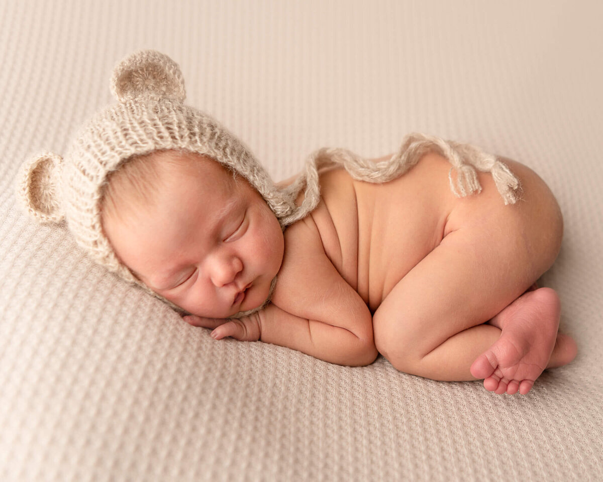 baby boy with bear bonnet in bum-up pose on beige