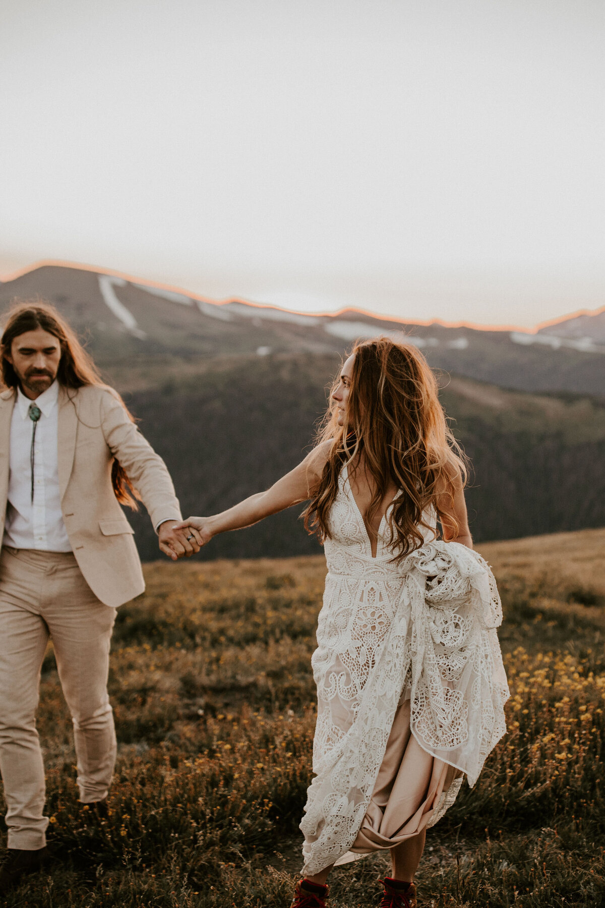 bride and groom wearing an ivory wedding gown and tuxedo pose holding hands in the mountains