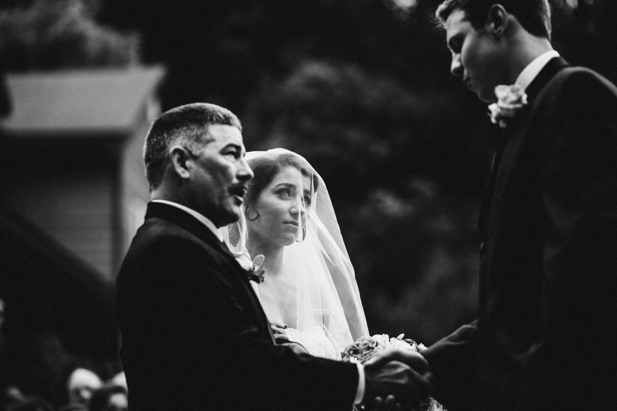 bride with tears in her eyes looks at groom who shakes father's hand