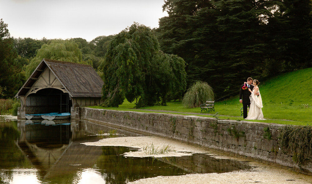 Boho bride standing with her groom beside the boathouse in Castle Leslie Estate