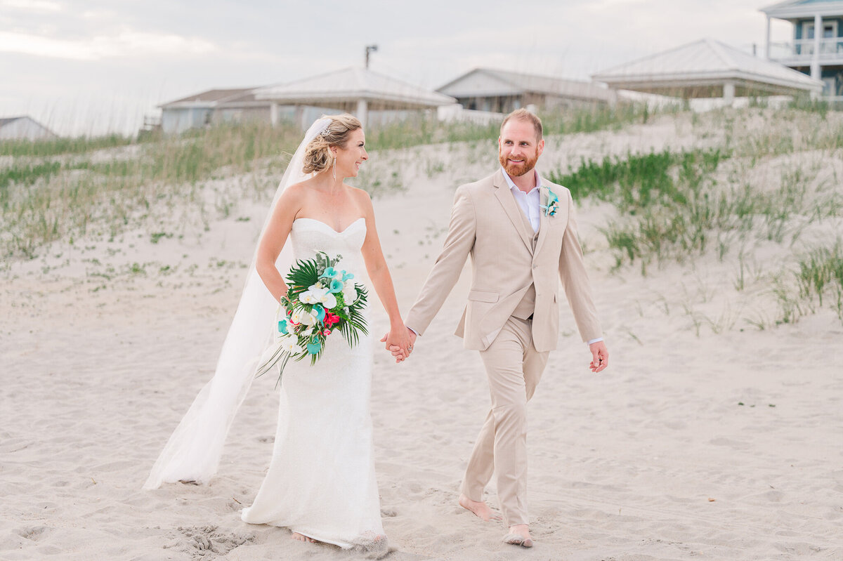 A loving newly married couple walking downt the beach after their wedding ceremony enjoying their Raleigh wedding photography session by JoLynn Photography
