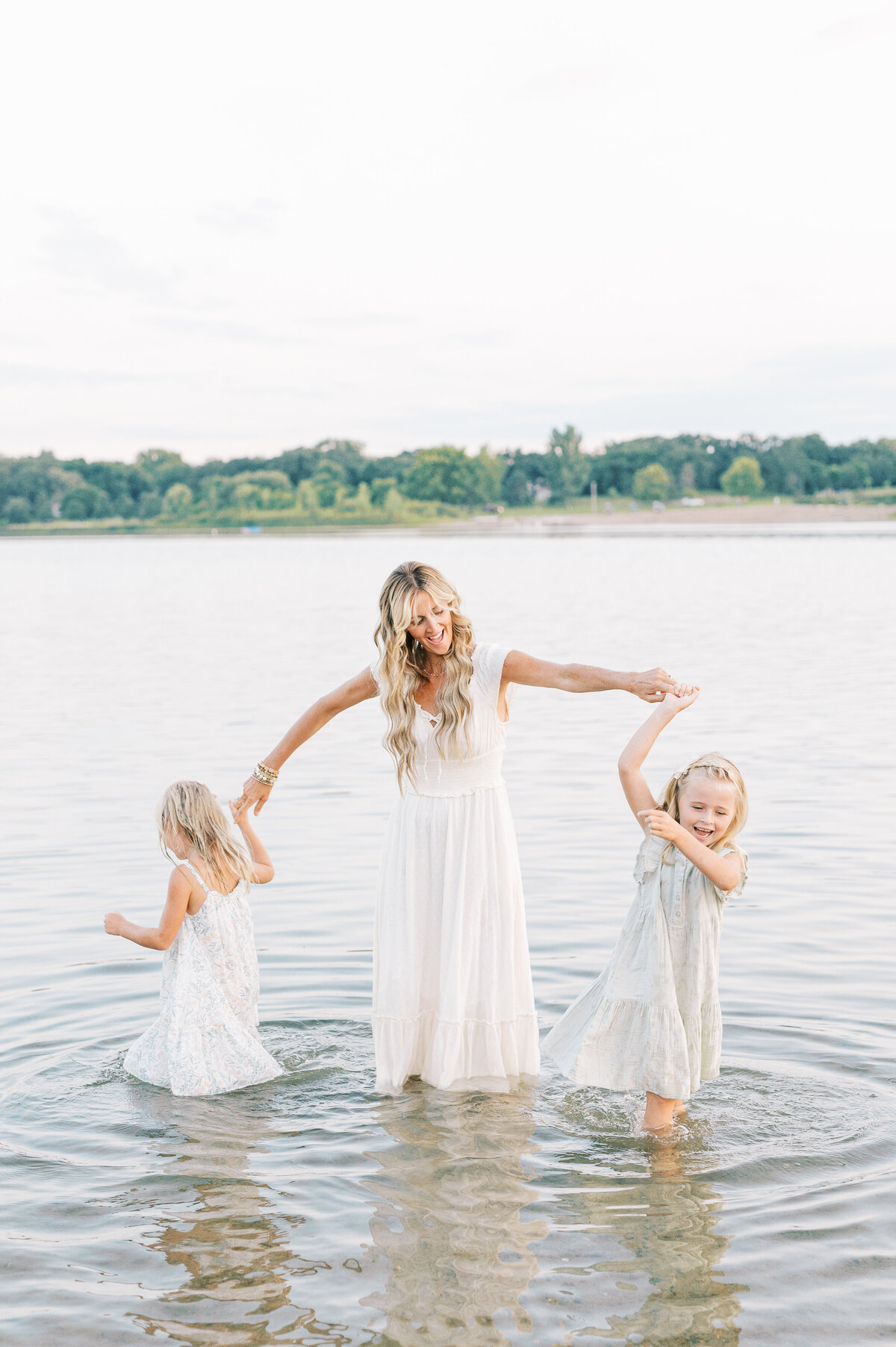Mom twirling daughter's in water at sunset