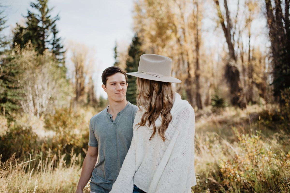 Photographers Jackson Hole capture woman wearing hat and walking through forest with fiance