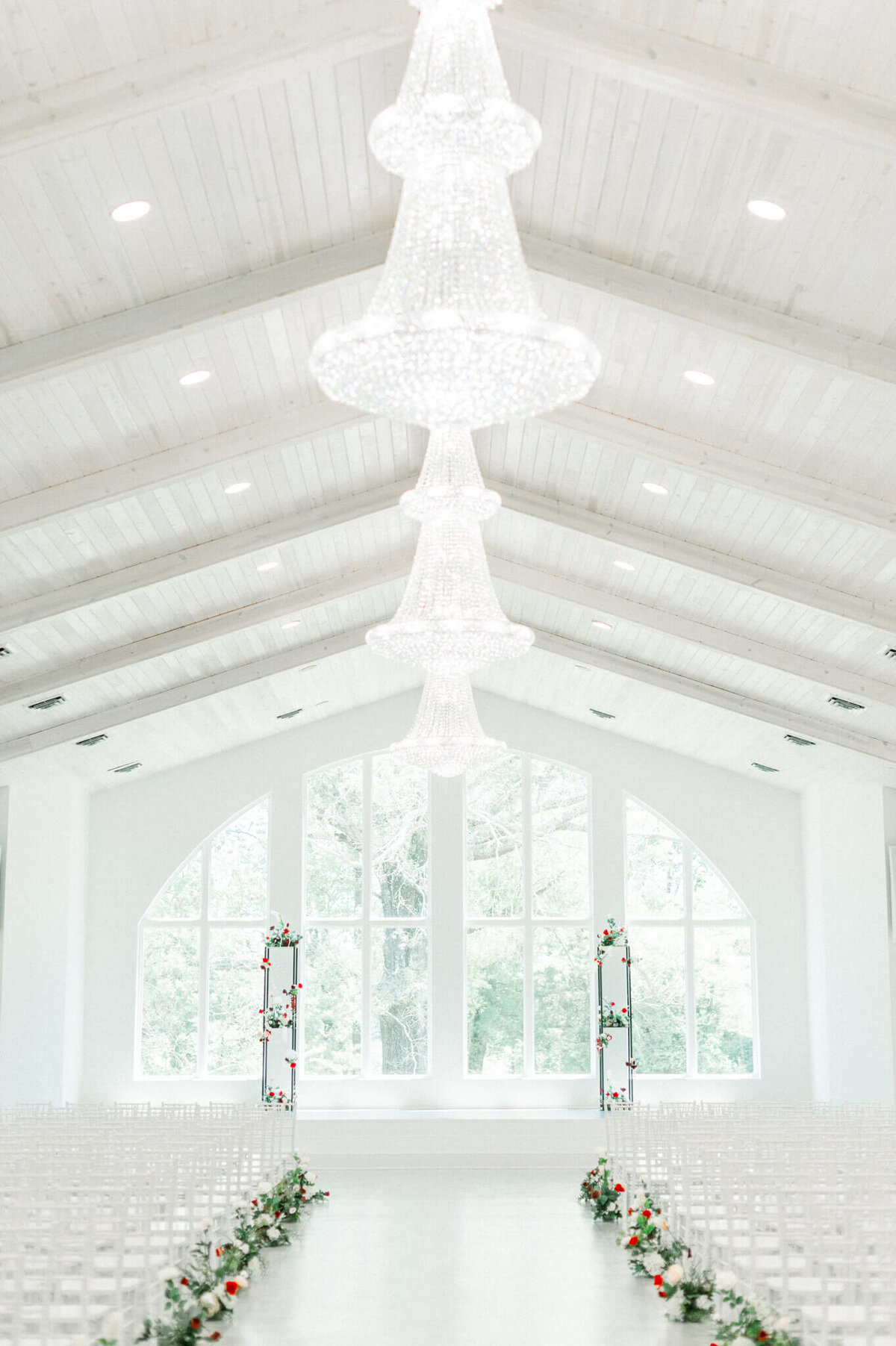 interior photo of all-white wedding venue with large windows and glass chandeliers