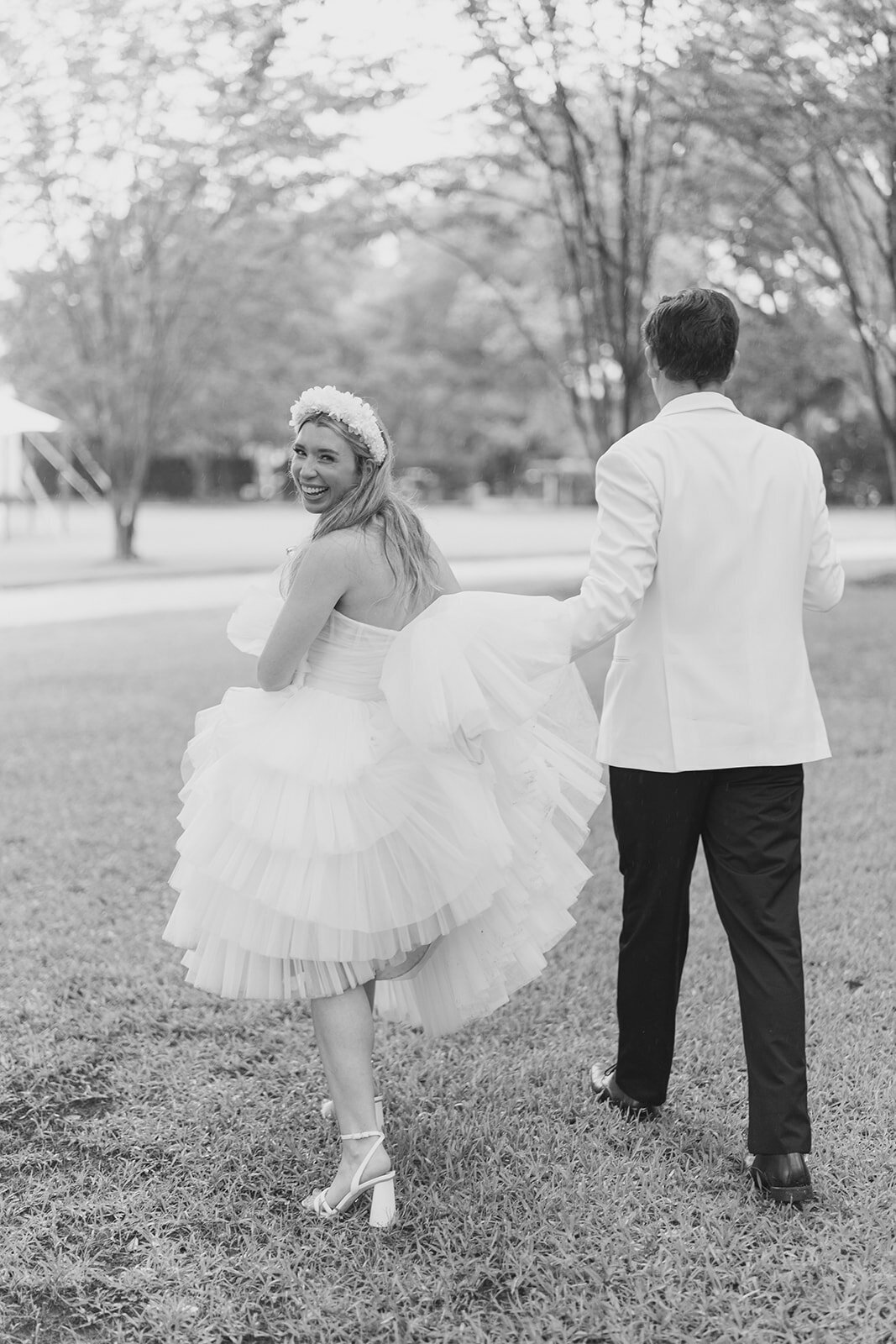Bride in layered tulle dress. Groom in white tuxedo jacket helping bride with dress during Lowndes Grove wedding. Kailee DiMeglio Photography.